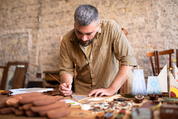 Middle aged wood carpenter works on his project. Concentrated joiner draws his future models.