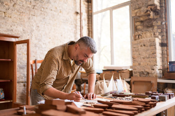 A joiner in flanel shirt during his work with the project. A craftsman sketches the sails for his wooden boats.