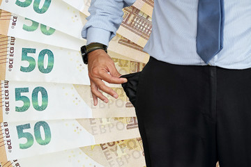 Close-up of hand of senior businessman in suit turning pocket of his trousers inside out and showing it empty. Crisis, unemployment, bankruptcy concept. Background of 50 euro in the background.