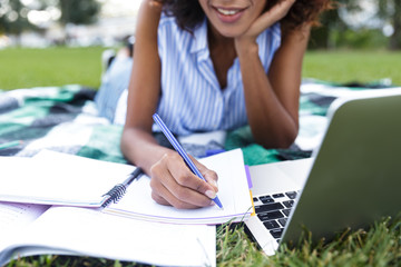 Obraz premium Happy smiling young girl doing homework using laptop outdoors in park.