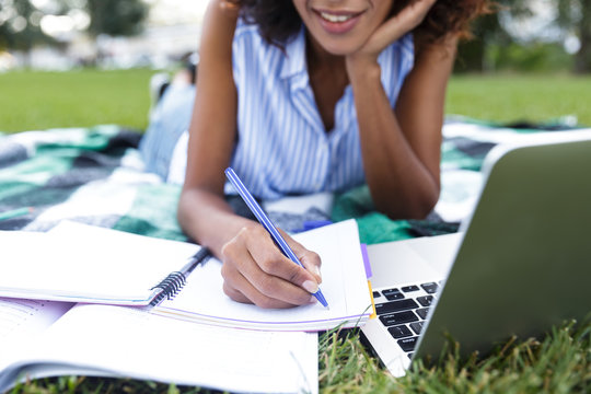 Happy smiling young girl doing homework using laptop outdoors in park.