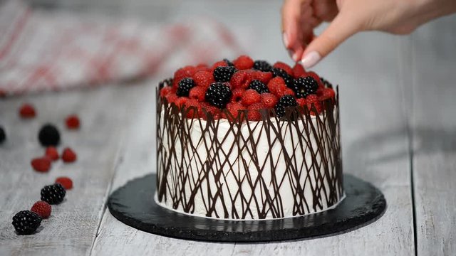 Pastry chef decorates a cake with berries.