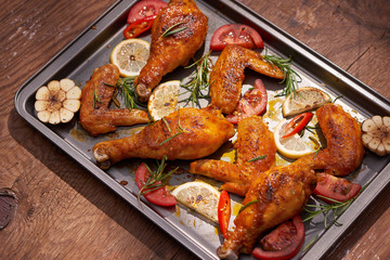 Baked chicken drumstick and wings on baking tray over dark wooden background.