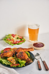 Grilled chicken legs roasted on the grill on dark plate with tomato sauce in a bowl and lettuce leaves, glass mug of beer
