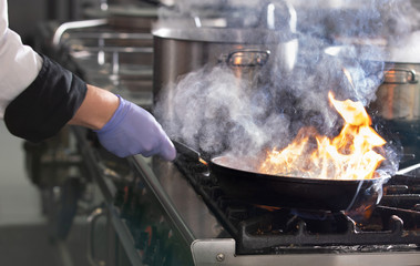 Chef in restaurant kitchen at stove with pan, cooking food
