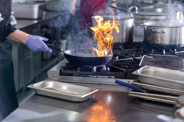 Chef in restaurant kitchen at stove with pan, cooking food
