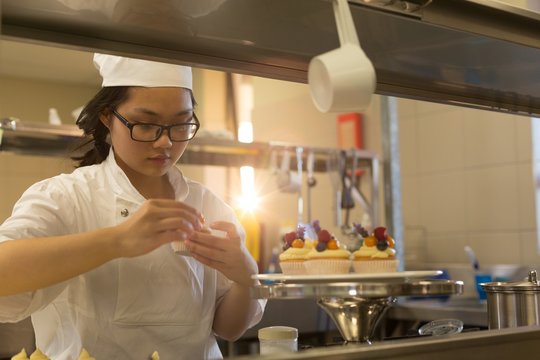 Female chef garnishing muffins in kitchen