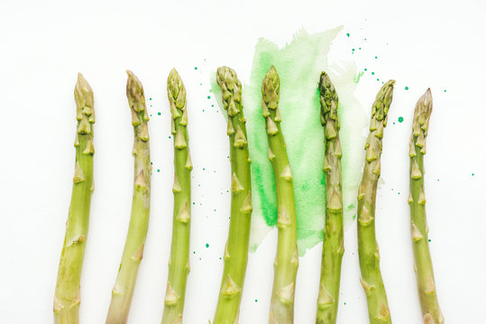 top view of row of ripe asparagus stems on white surface with green watercolor strokes