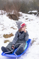 portrait of a boy sitting in a toboggan waiting to go sledding