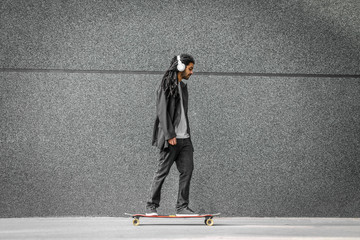 Young urban dreadlocks hipster man riding on his long board and listening to the music. Riding on...