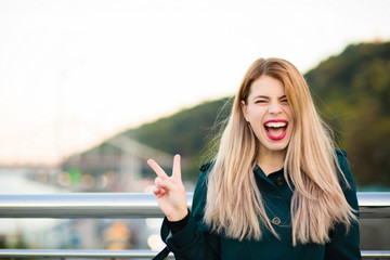 Emotional blonde model wearing green coat showing peace gasture. Space for text
