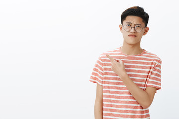 Displeased smart young attractive asian male student in glasses and t-shirt raising eyebrow in...