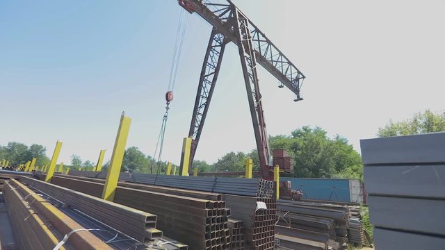 A large yellow gantry crane moves around the warehouse with metal, a gantry crane against the blue sky