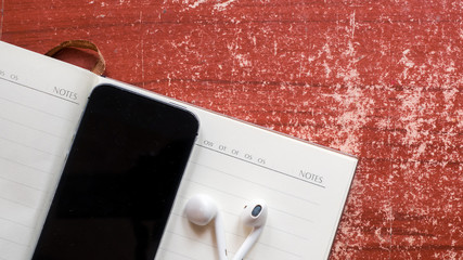 earphones and smartphone with notebook on wood table.