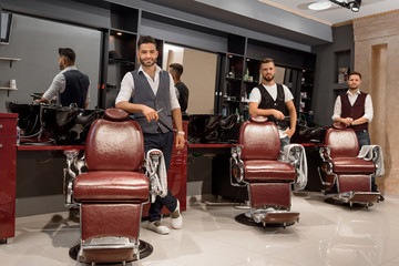 Confident masters barbers standing near hairdresser chairs and posing.