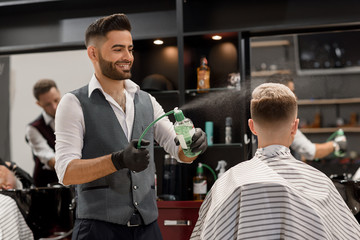 Smiling barber sprinkling water on client's haircut using sprayer bottle.