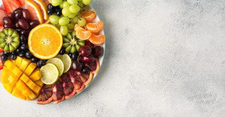 Raw fruits berries assortment platter on the white plate, on the off white table, top view, copy space