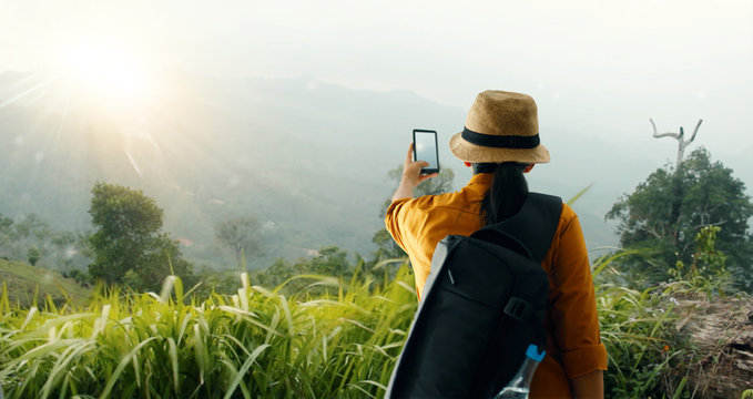 Backpacker using smartphone taking a photo of  beautiful landscape on mountain peak while exploring, trekking in tropical rain forest of Asia