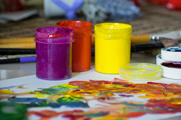 A jars of paint, with paint stains on a white sheet of paper. Colorful gouache paints in jars.