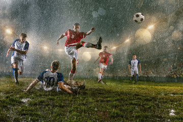 Soccer players performs an action play on a professional night rain stadium. Dirty players in rain...