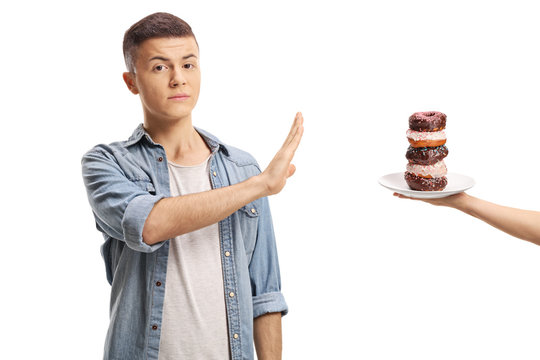 Teenage boy gesturing stop with his hand to a pile of donuts on a plate
