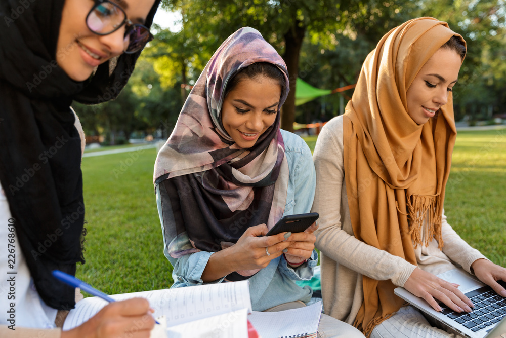 Canvas Prints Happy young arabian women students using laptop computer and mobile phone outdoors in park.