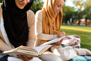 Happy young arabian women students writing in copybooks in park outdoors.
