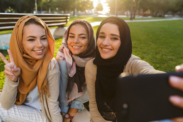 Arabian women students take selfie by phone in park outdoors.