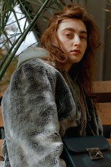 Street portrait of a beautiful and stylish girl in a fur coat, with coffee and a telephone