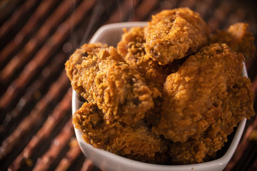 Bucket full of crispy kentucky fried chicken with smoke on brown background. Selective focus.