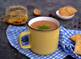 Soup puree from baked aubergines and tomatoes in a yellow mug. Served with feta cheese and crackers.