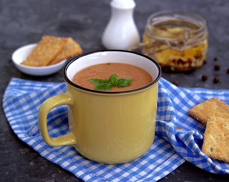 Soup puree from baked aubergines and tomatoes in a yellow mug. Served with feta cheese and crackers.