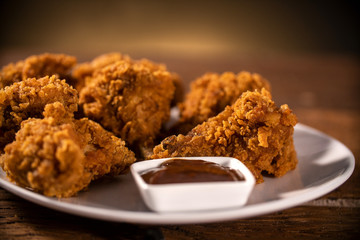 Bucket full of crispy kentucky fried chicken with smoke and barbecue sauce on brown background. Selective focus.
