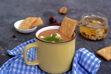 Soup puree from baked aubergines and tomatoes in a yellow mug. Served with feta cheese and crackers.