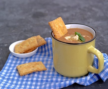 Soup puree from baked aubergines and tomatoes in a yellow mug. Served with feta cheese and crackers.