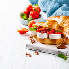 Fresh sandwich with croissant with goat cheese, strawberries, honey and pecans on wooden cutting board with copy space.