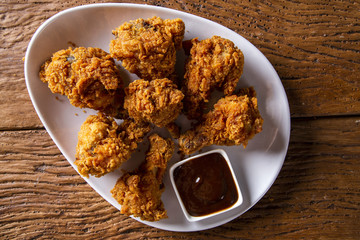 Bucket full of crispy kentucky fried chicken with smoke and barbecue sauce on brown background. Selective focus.