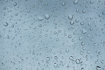 raindrops on glass window of car with cloudy sky in the background