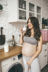 Pretty pregnant woman in kitchen having breakfast and cup of milk