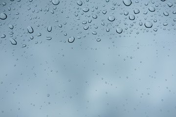Difference size of raindrops on glass window of car with cloudy sky in the background