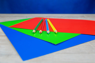 Colorful pencils and sheets of paper on white wooden desk and dark blue background