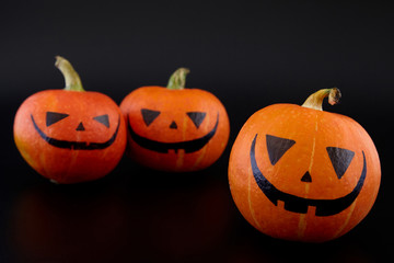 Pumpkins with painted faces on black background. Halloween backdrop.