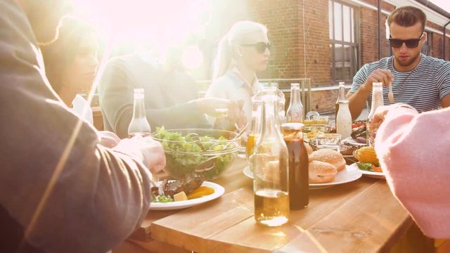 leisure and people concept - happy friends having dinner or bbq party and eating on rooftop in summer