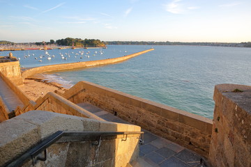 The ramparts of the walled city of Saint Malo at sunset, with the pier (Mole des Noires) and the harbor in the background, Saint Malo, Brittany, France