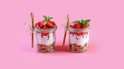 Dessert in a glass with granola, yogurt and strawberries. Useful breakfast. isolated on pink background. Authentic lifestyle image. copy space