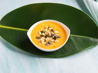 Pumpkin creamy soup served on green leaf. Served with squash seeds and cashew
