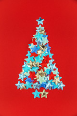 Christmas tree of colored small stars on bright red background in flat lay style