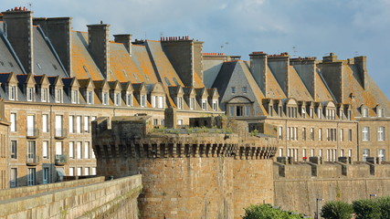 Traditional house facades with chimneys and roofs, located inside the walled city of Saint Malo, with the ramparts in the foreground, Saint Malo, Brittany, France - obrazy, fototapety, plakaty
