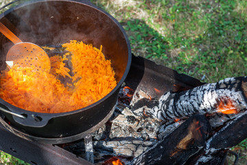Carrots are cooking in the pot on the fire for rice pilau. Camping in the nature and preparing food concept