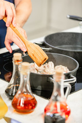 Man cooks meat in a frying pan. Hand using spatula to stir red and white frying pan full of meat